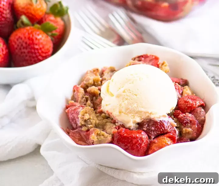 bowl of strawberry crumble topped with ice cream with a bowl of fresh strawberries in the background