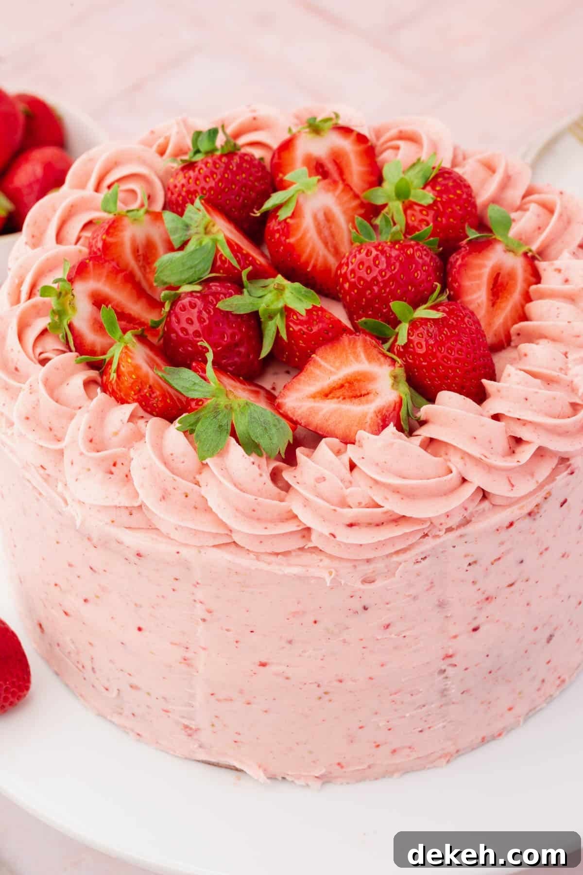 A whole uncut gluten-free strawberry cake frosted with strawberry buttercream piping and halved strawberries.