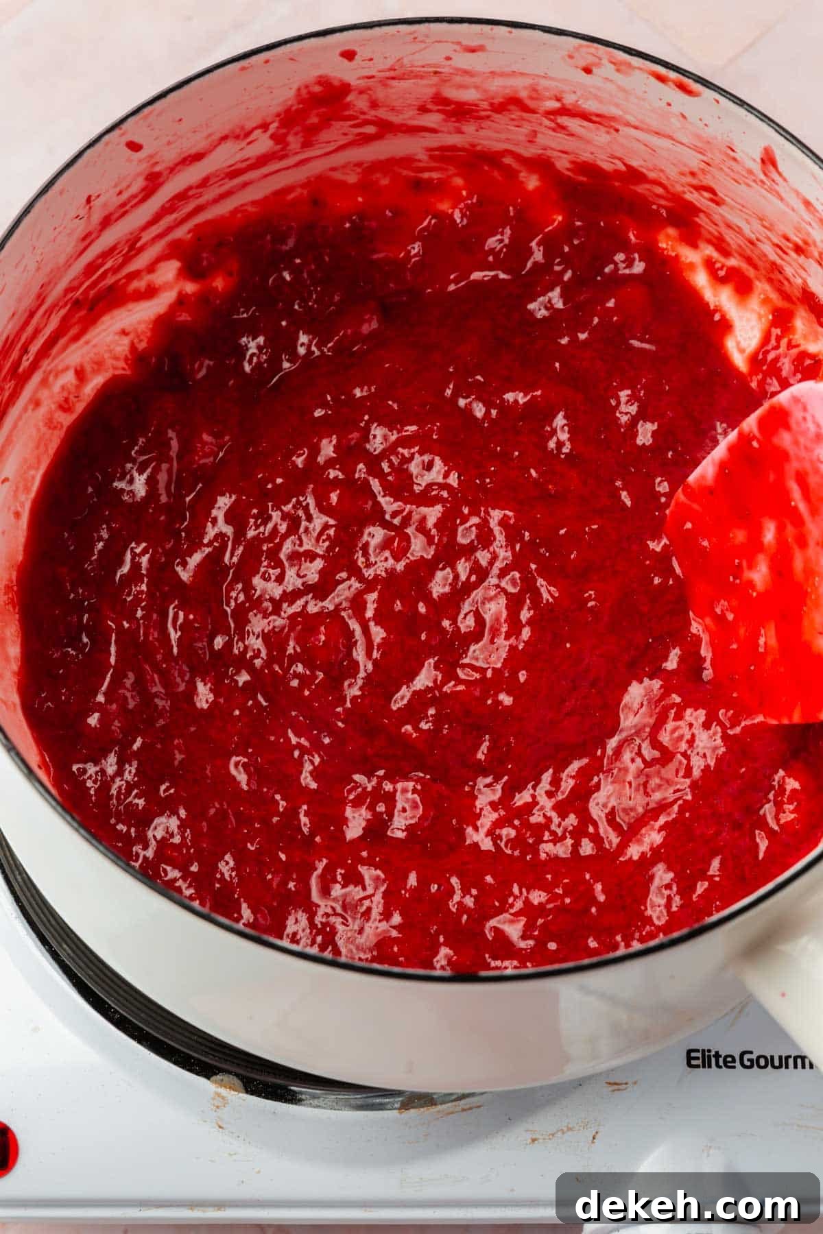 A white saucepan with a pureed strawberry reduction in it.