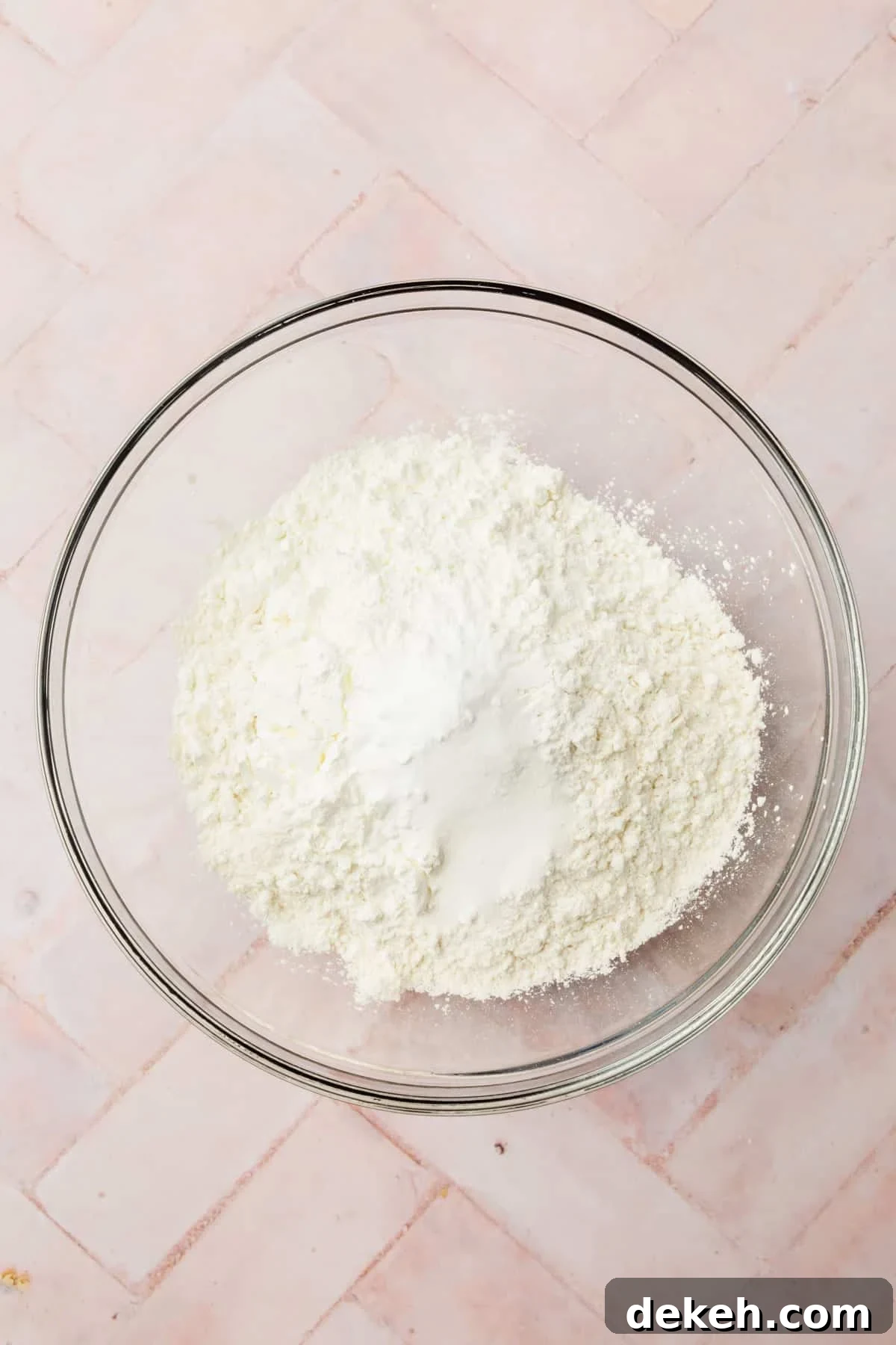 A glass mixing bowl with gluten-free flour blend, cornstarch, salt, baking powder, and baking soda in it before mixing.