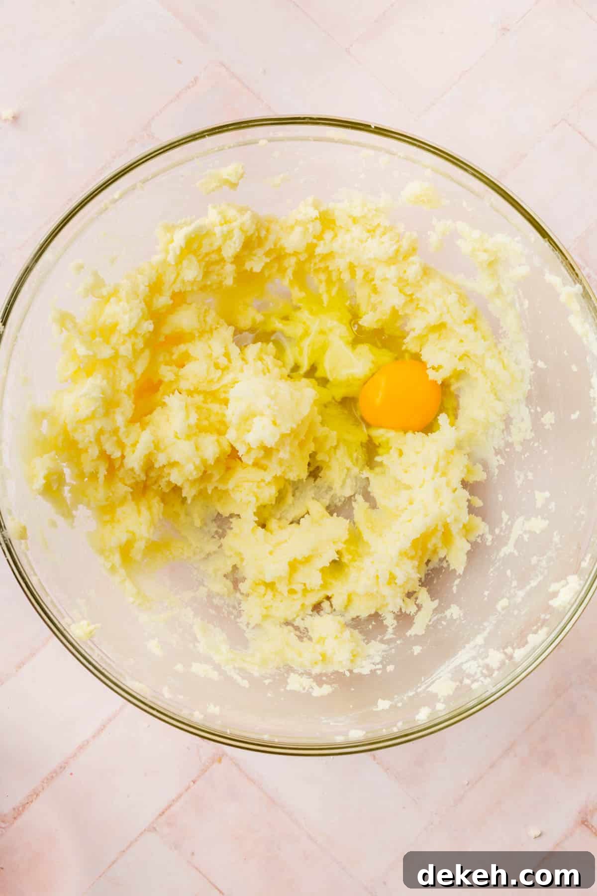 A glass mixing bowl with a creamed butter and sugar mixture topped with an egg.