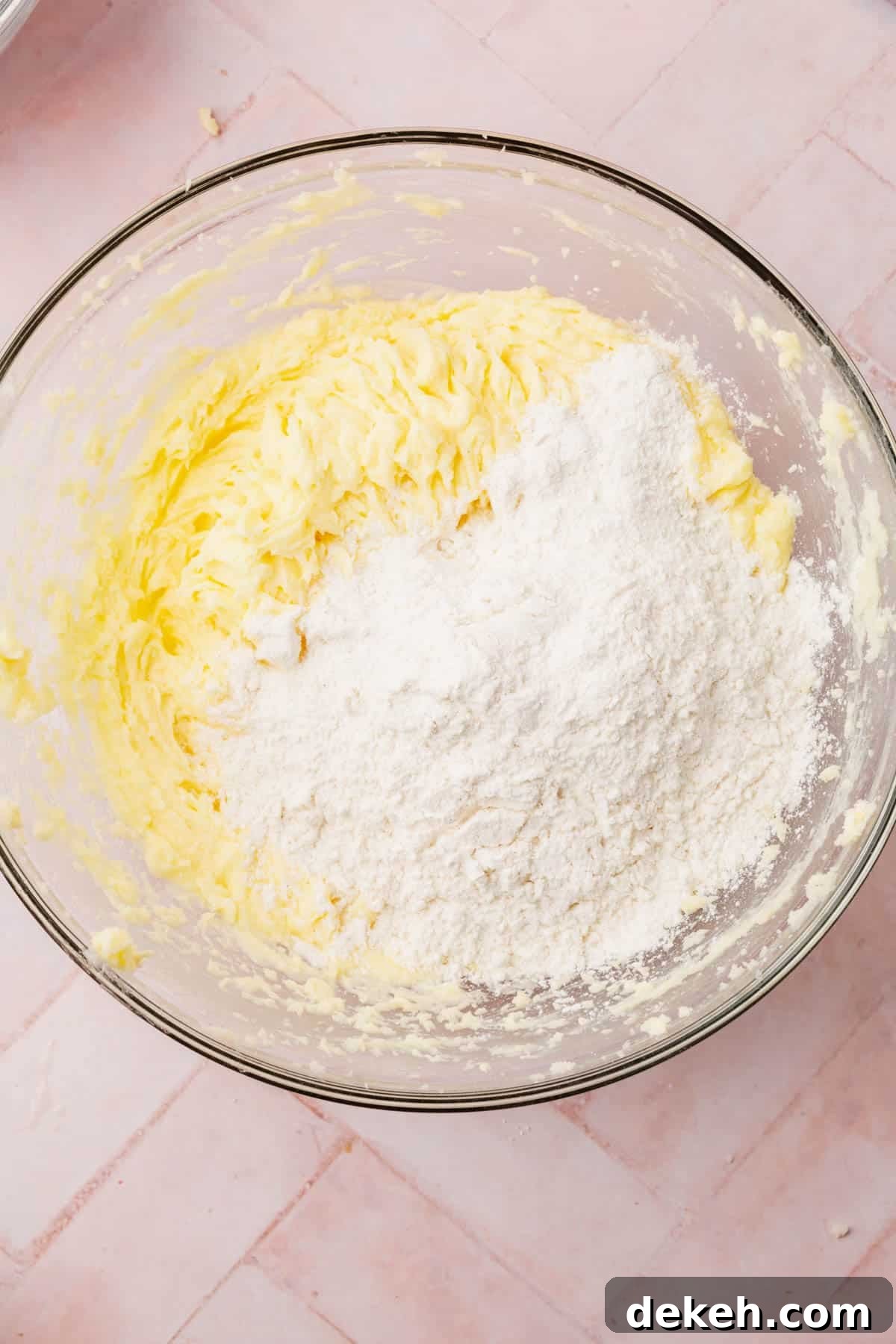 A glass mixing bowl with a creamed butter and sugar mixture topped with gluten-free flour blend.