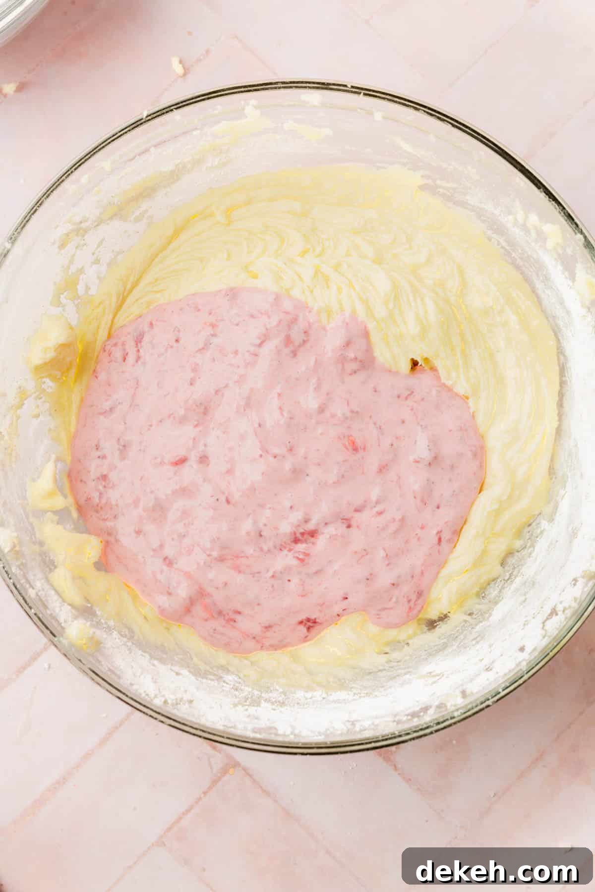 A vanilla cake batter in a mixing bowl topped with a strawberry sour cream mixture.
