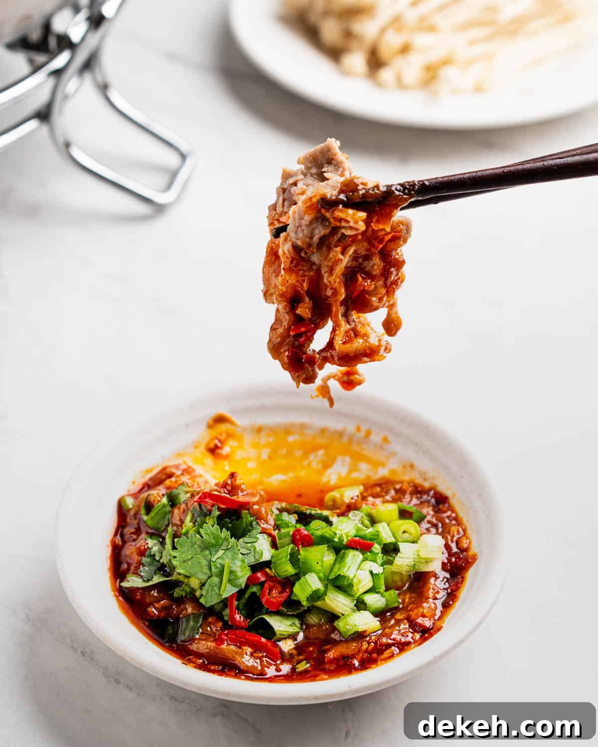 Chopsticks dipping meat into spicy peanut sauce.