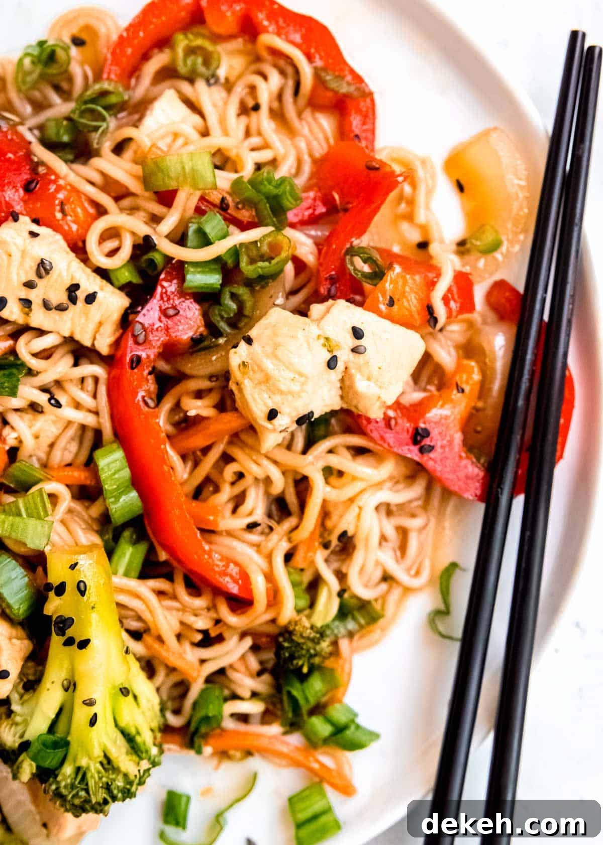 a white plate filled with stir fry with shirataki noodles, red peppers, broccoli, carrots, and onions; chopsticks on the side