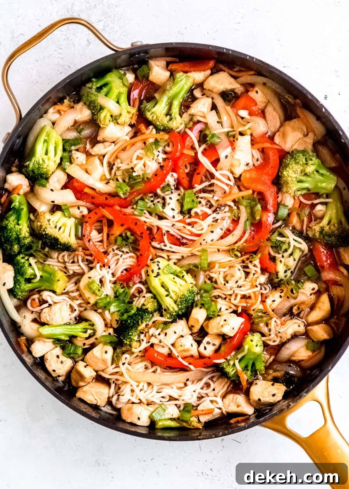 an overhead shot of a large skillet filled with shirataki chicken stir fry garnished with green onions and sesame seeds