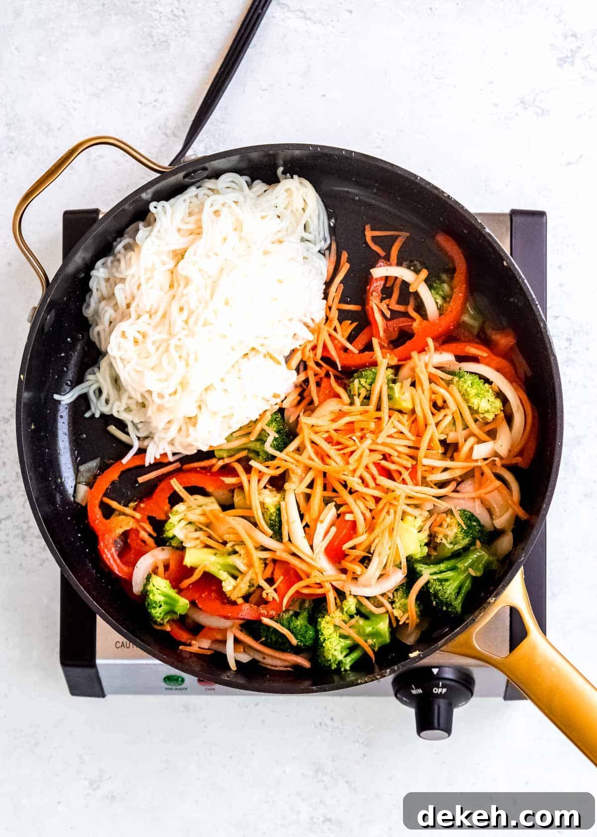 shirataki noodles and shredded carrots in a skillet with sauteed red peppers, onions, and broccoli
