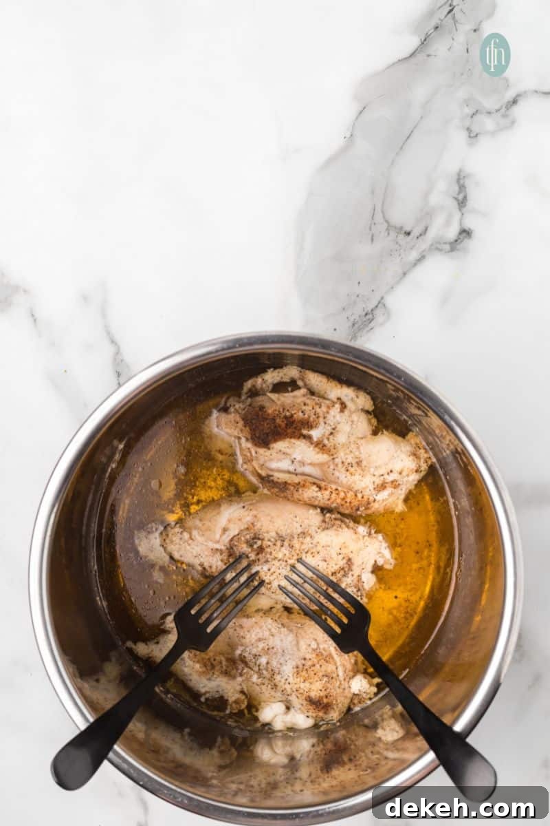 A bowl of cooked chicken with a liquid mixture and 2 forks.