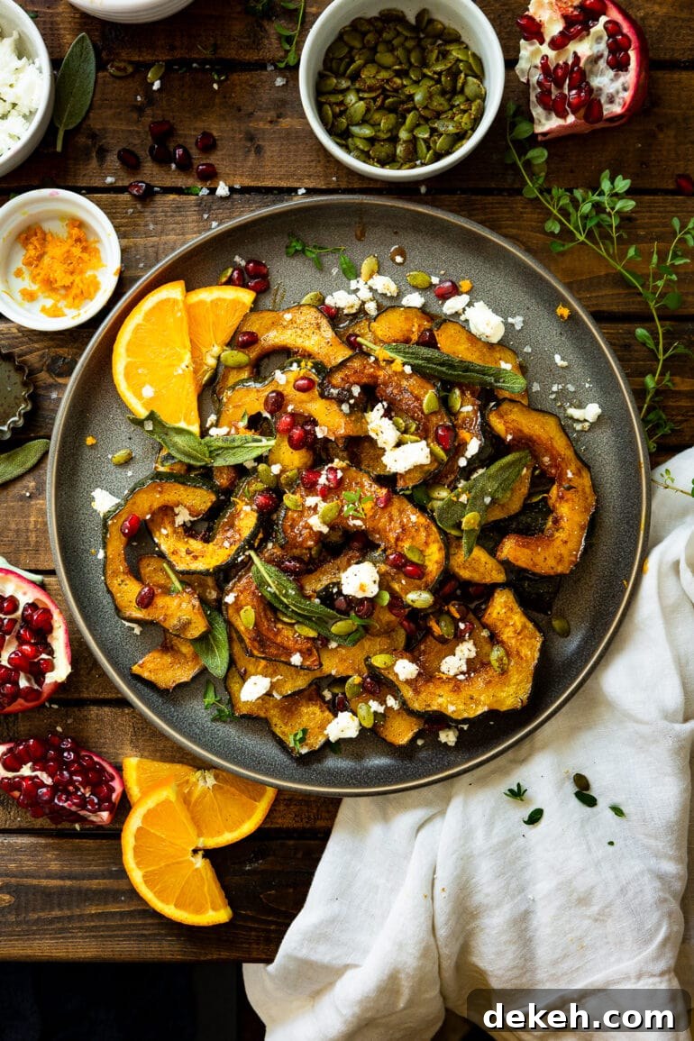 a photo of a large serving plate full of holiday acorn squash topped with feta, crispy sage leaves and pomegranate seeds with orange slices on the side