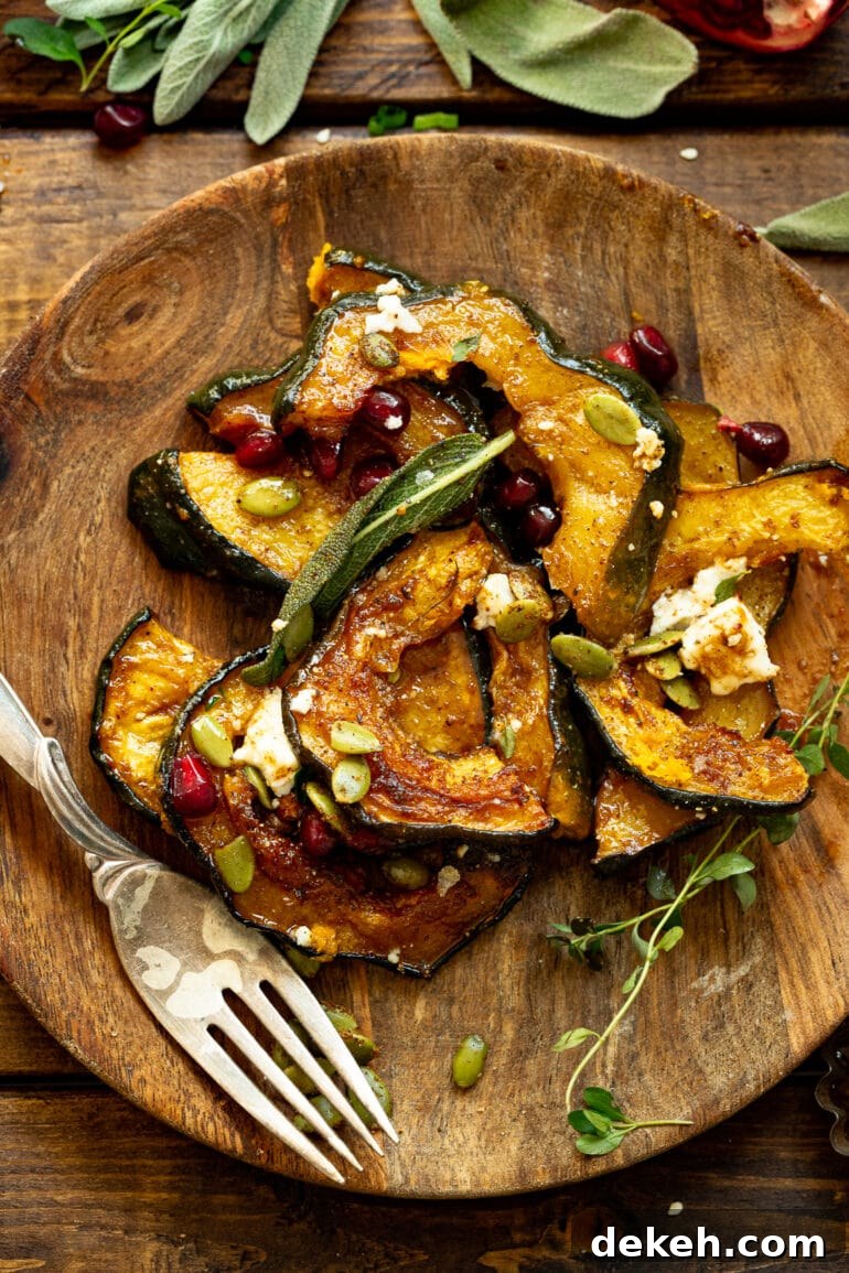 a photo of several slices of roasted acorn squash on a wooden plate topped with feta, pomegranate seeds, pepitas and fried sage.