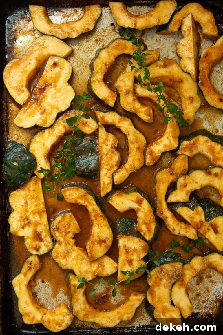 a photo of uncooked acorn slices coated in seasonings scattered on a baking sheet.