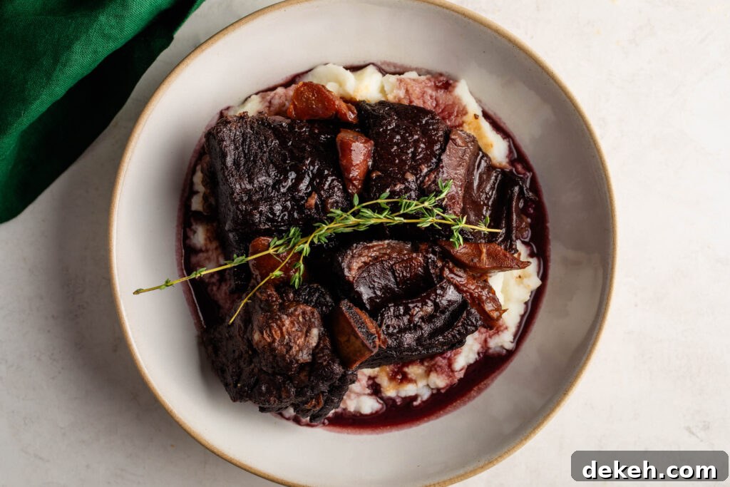 bowl of braised beef short ribs over a bed of mashed potatoes garnished with a sprig of thyme