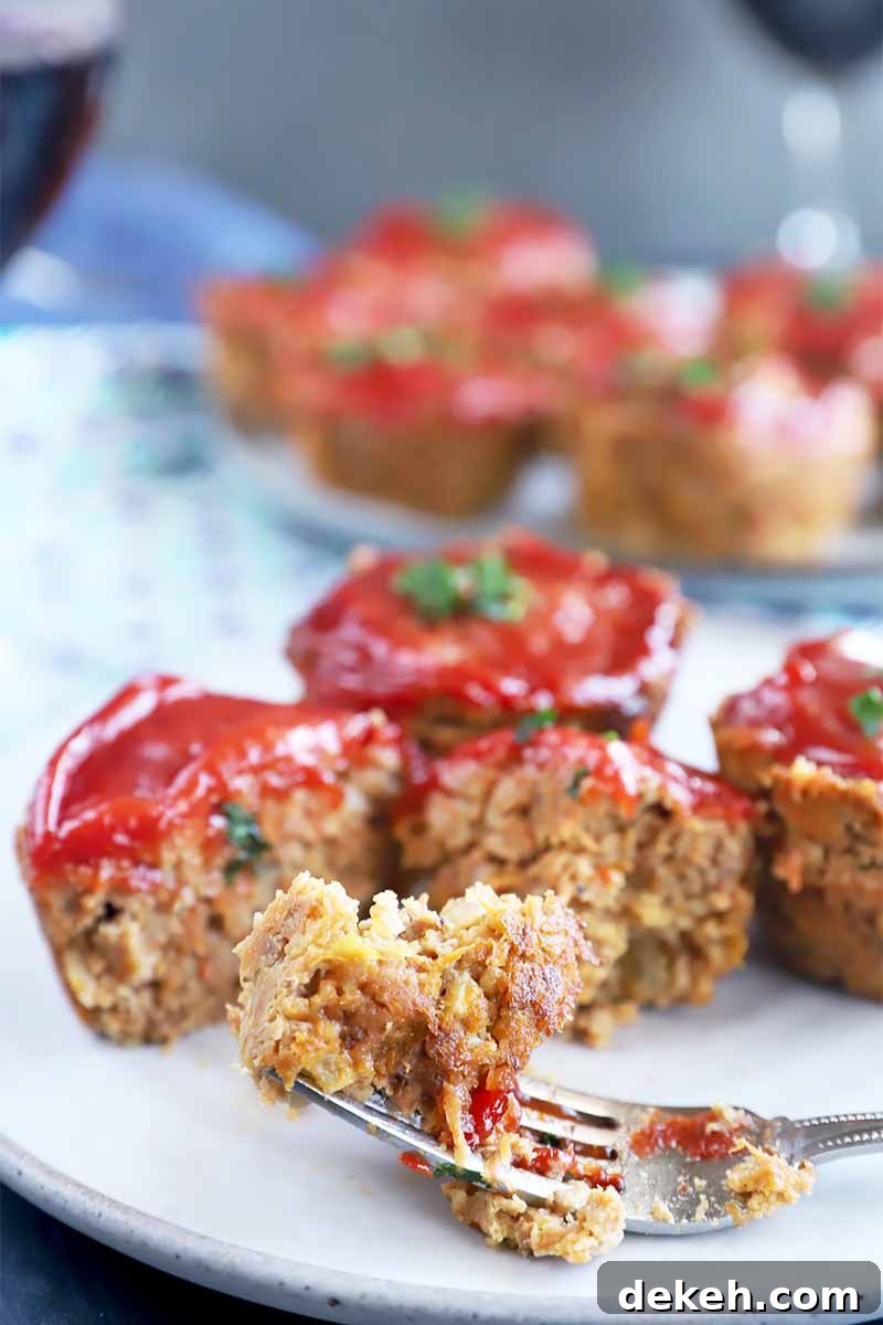 Vertical image of a fork taking pieces from small meatloaf muffins topped with ketchup.