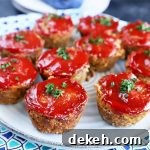 Horizontal image of small ground beef rounds baked and topped with ketchup on a blue plate.