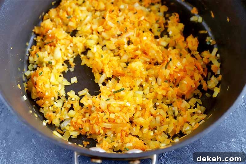 Horizontal image of grated carrots and chopped onions cooking together in a pot.