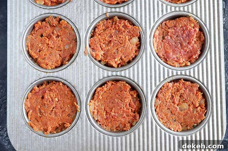 Horizontal image of a muffin pan filled with a seasoned ground beef mixture.