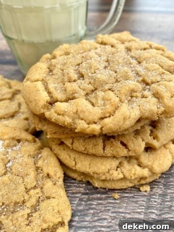 A short stack of peanut butter cookies next to a small glass of milk.