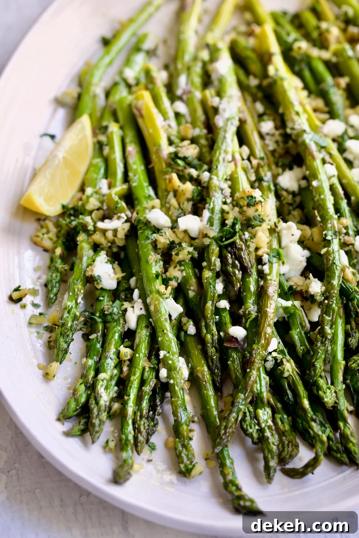Roasted Asparagus with Walnut Lemon Gremolata and Goat Cheese on white oval platter with lemon wedge.