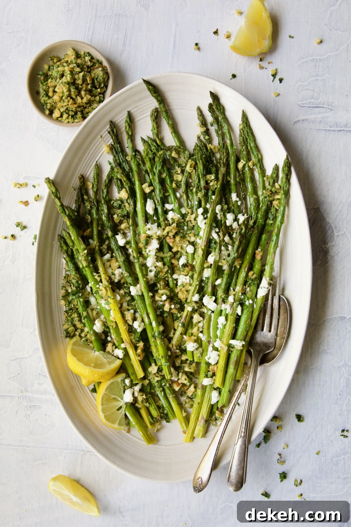 Roasted Asparagus with Walnut Lemon Gremolata and Goat Cheese with lemon wedges, serving utensils and bowl of gremolata.