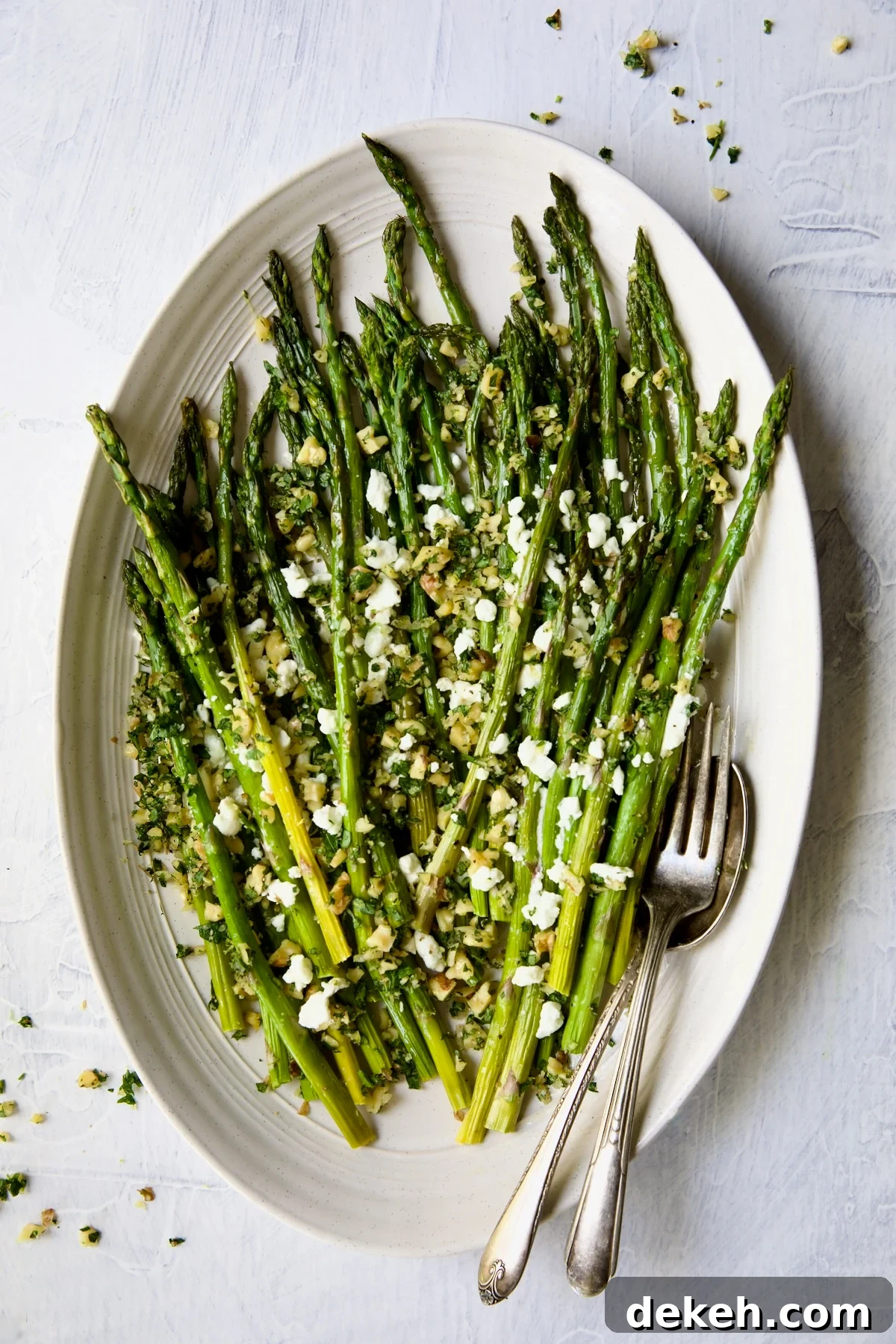 Roasted Asparagus with Walnut Lemon Gremolata and Goat Cheese on white oval platter.