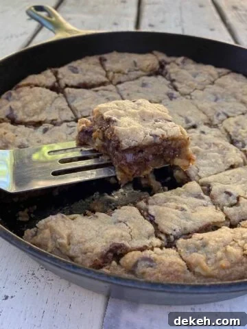 Chocolate chip bar cookie on a spatula, lifted out of a cast iron skillet.