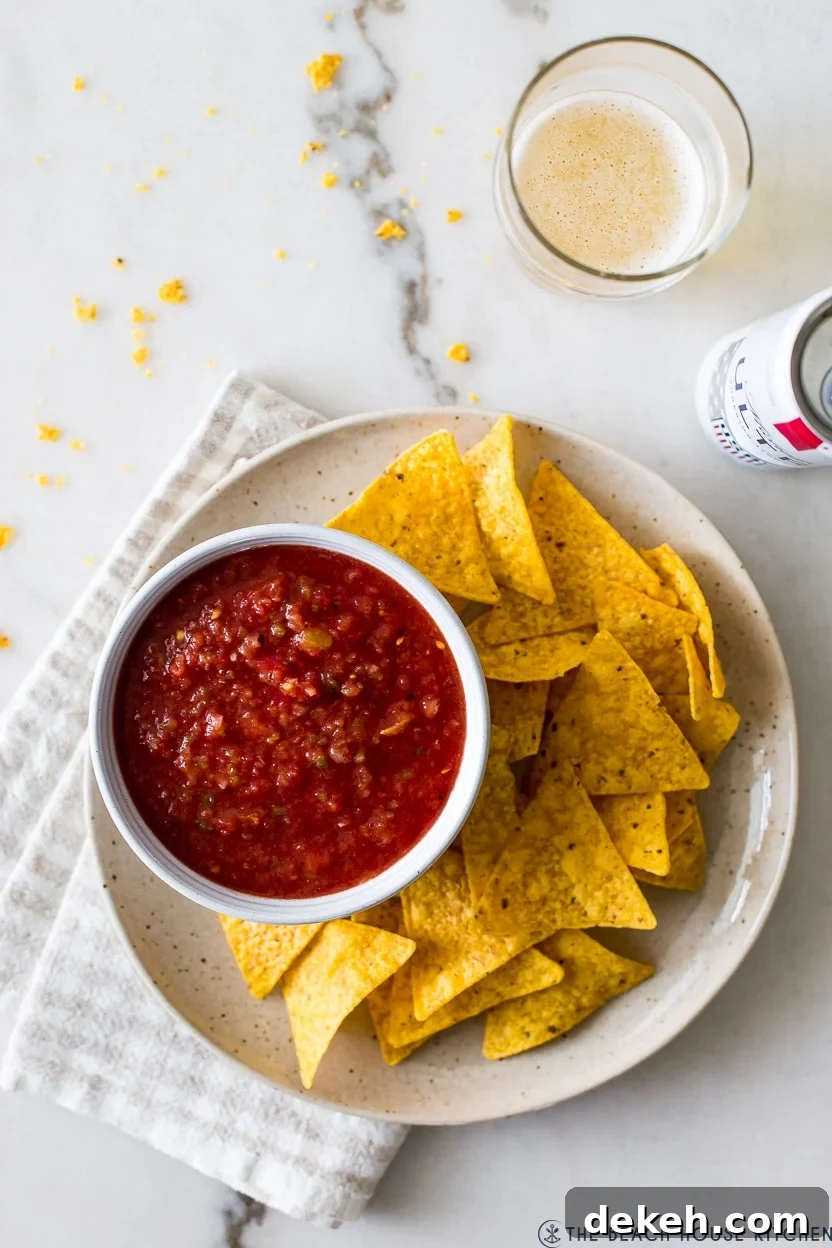 Overhead photo of a bowl of salsa on a plate with tortilla chips with a glass of beer off to the side