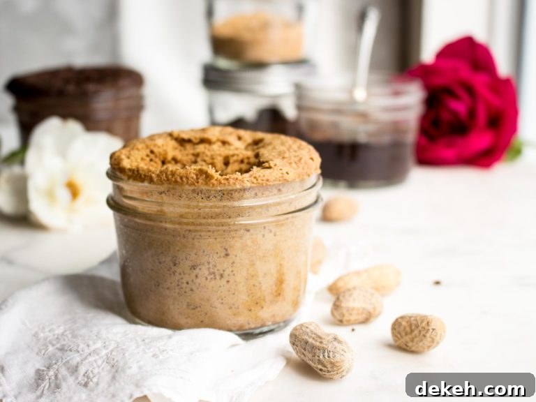 keto peanut butter mug cake in a jar with peanuts and chocolate peanut butter mug cakes behind