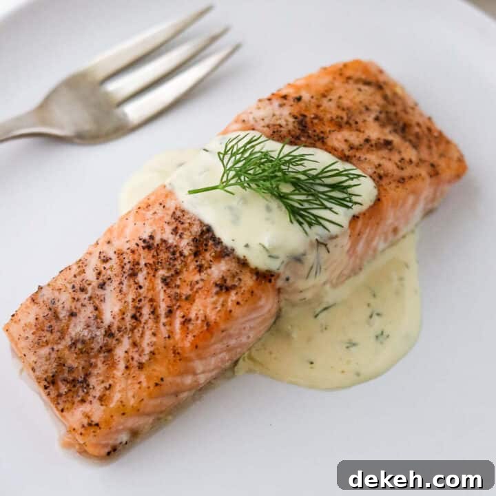 Close up of baked salmon topped with Warm Mustard Dill Sauce and a sprig of dill.