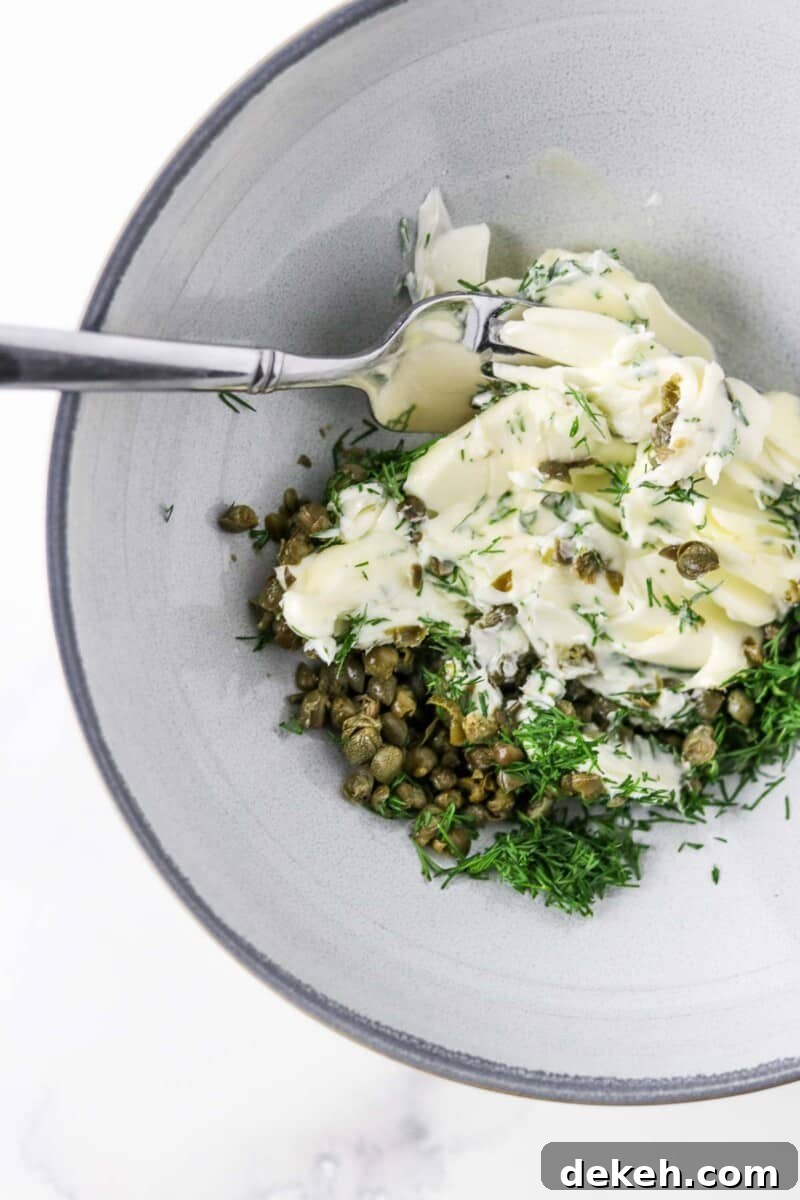 Butter, dill and capers together in a bowl with a fork.