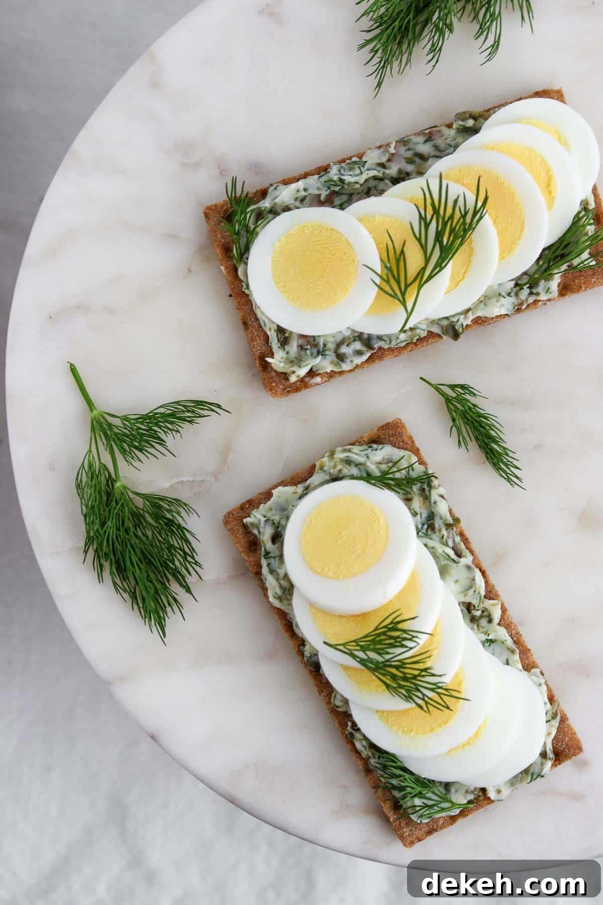 Overhead view of crispbread spread with dill caper butter and toped with hard-boiled egg and sprigs of dill.