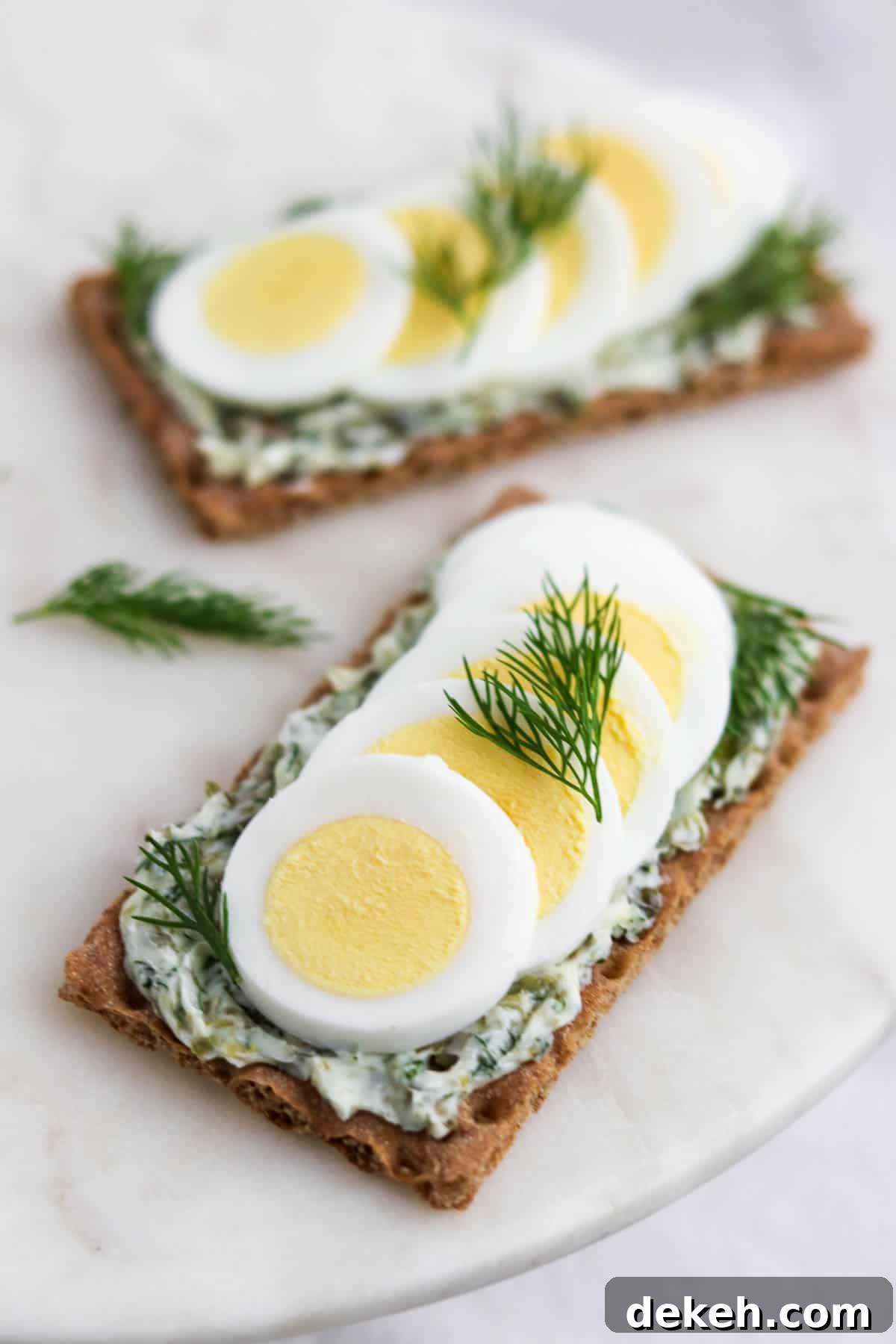 Crispbread topped with dill caper butter and slices of hard-boiled egg and dill sprigs.