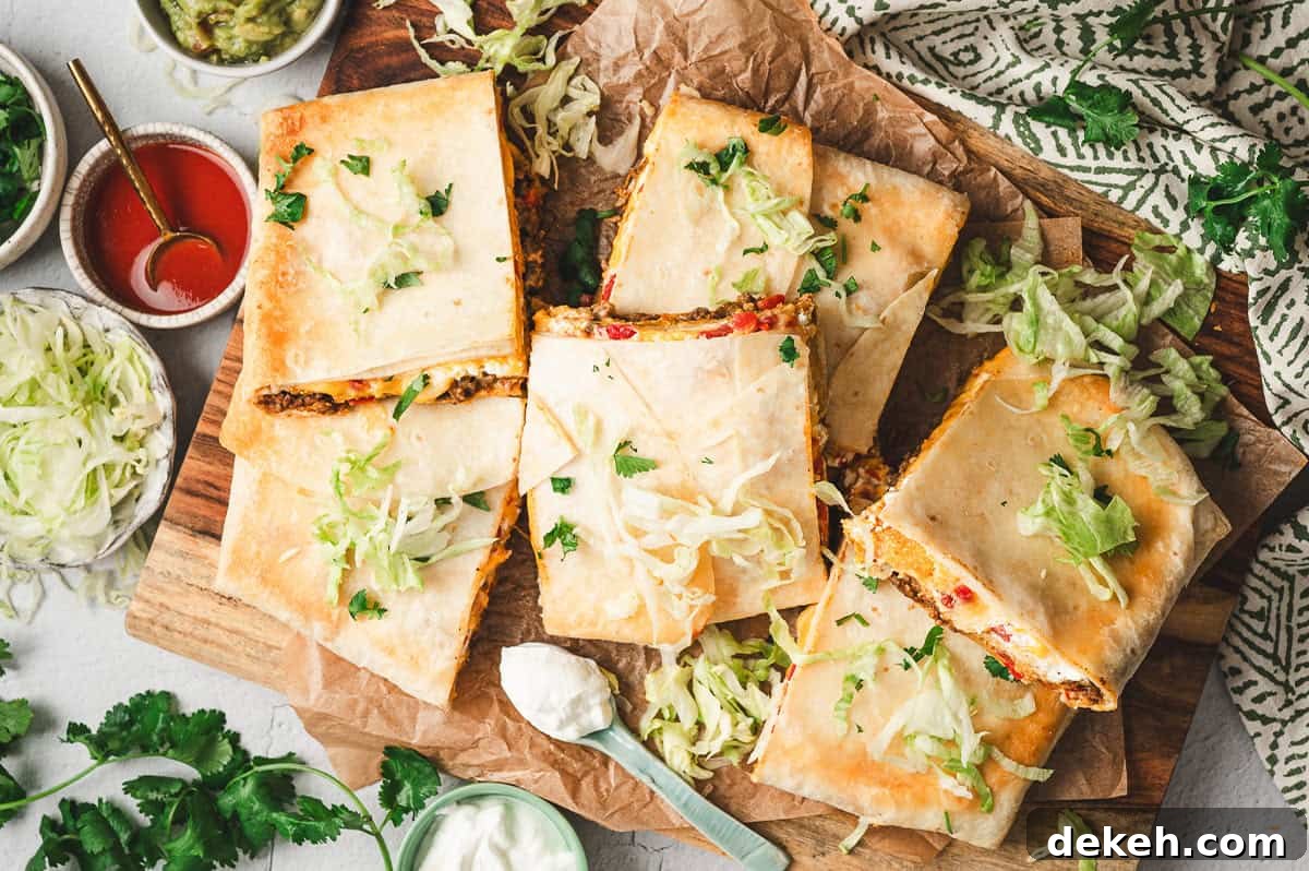 Overhead view of baked Crunchwrap Casserole cut into squares on a wooden board, topped with shredded lettuce and cilantro, surrounded by bowls of guacamole, sour cream, and hot sauce.