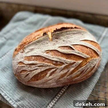 Artisan sourdough bread loaf with decorative scoring on a towel cooling on a rack.