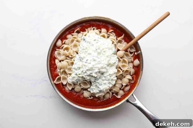 Tomato sauce, cheeses, and pasta in a pan.