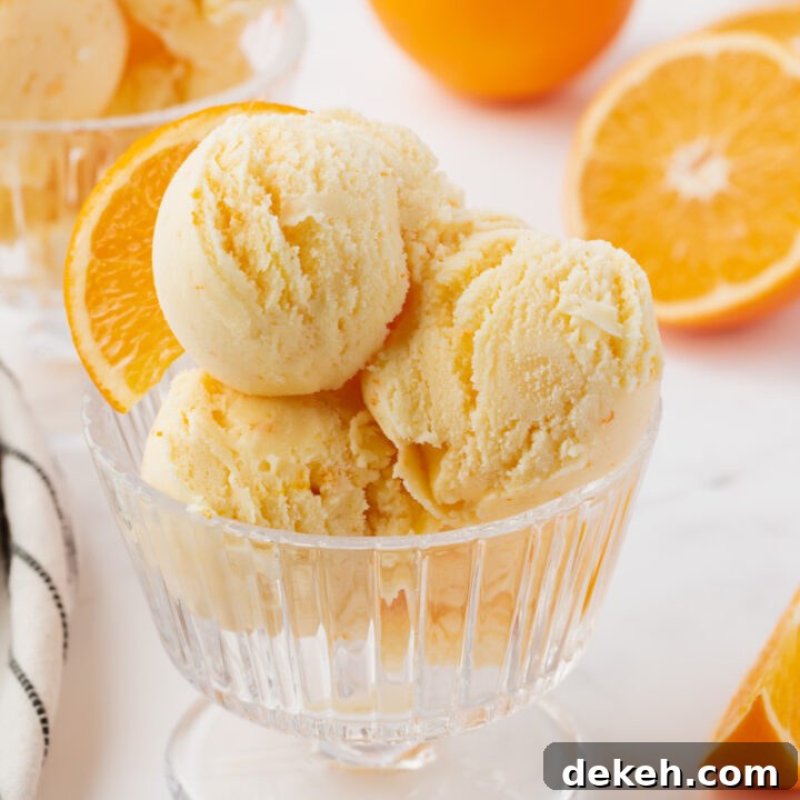 a ridged glass ice cream dish filled with scoops of homemade orange ice cream, garnished with an orange slice.