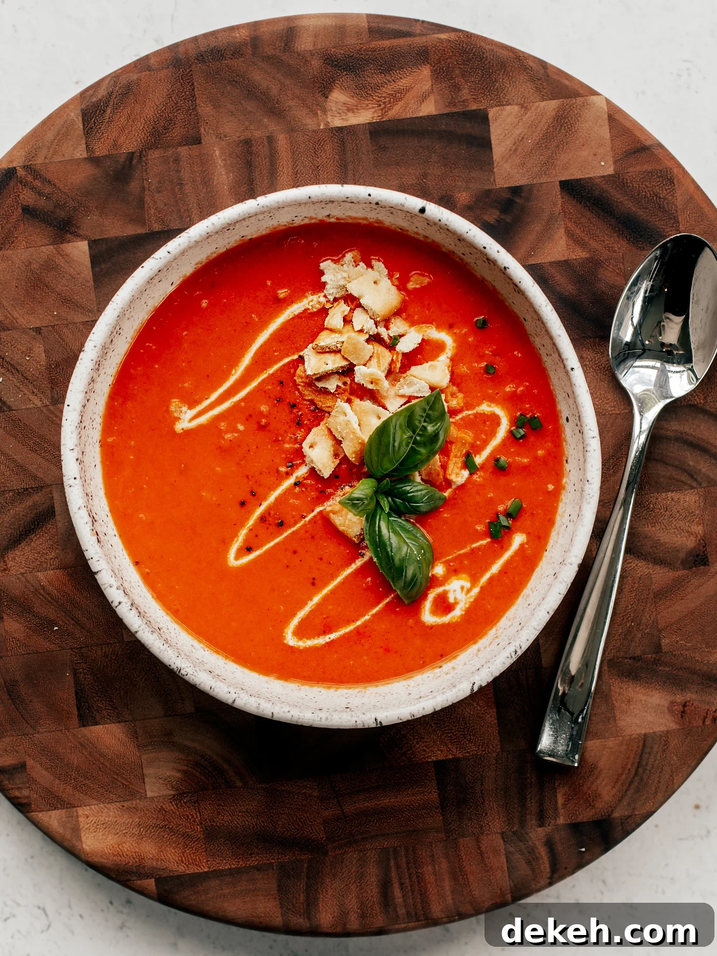 Creamy Homemade Tomato Soup Recipe with Basil and Garlic 3 Bowl of tomato soup with cream drizzle, crushed crackers, and basil leaves.