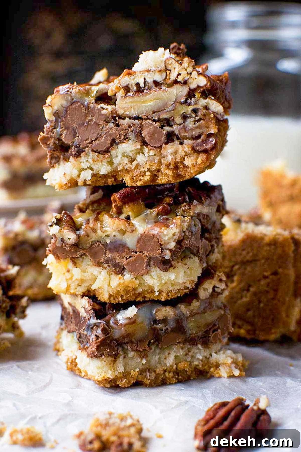 No-Bake Peanut Butter Crunch Bars — 6 Ingredients 10 A stack of three easy-to-make 7 layer bars with layers of graham cracker, coconut, chocolate, nuts and condensed milk on baking paper.