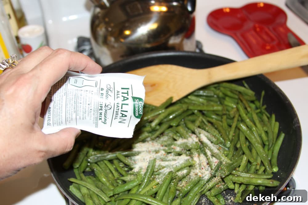 Green Beans Seasoned with Italian Dressing Sautéed green beans in a black frypan with Good Seasons Italian dressing mix being added