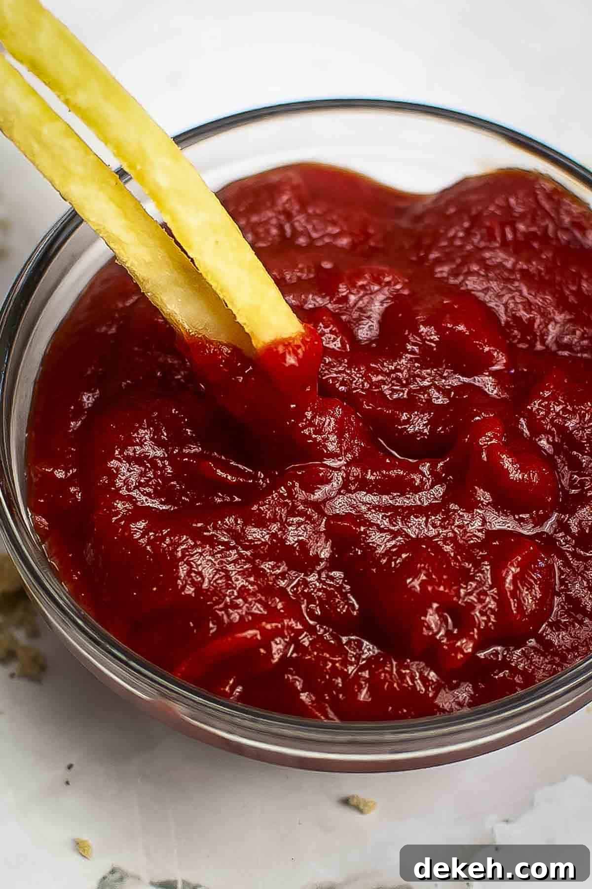 Homemade Tomato Ketchup Recipe from Scratch 2 Close up shot of two french fries being dipped into homemade ketchup in a clear bowl.