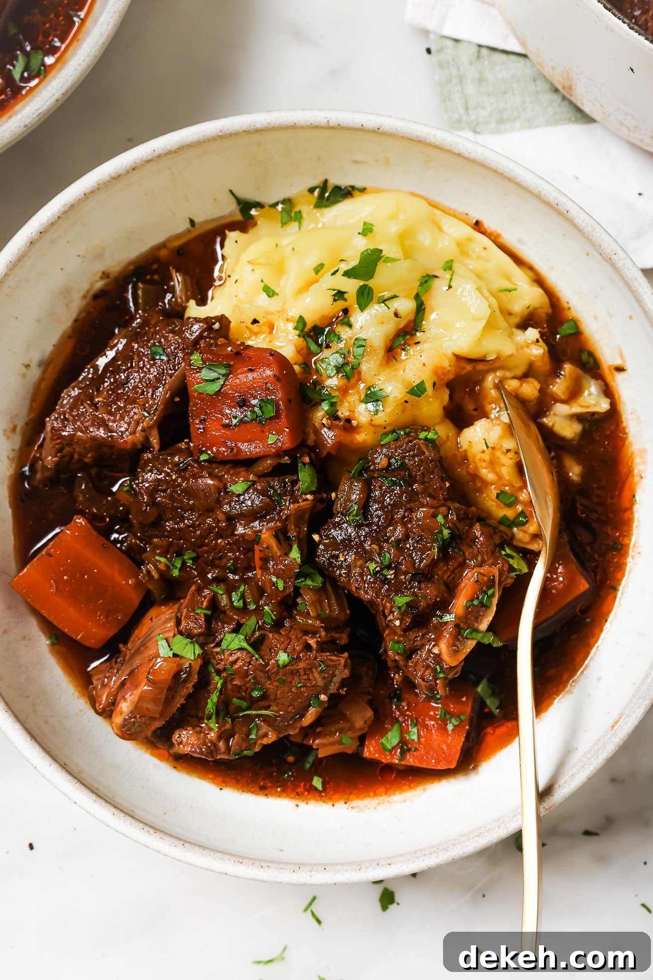 Tender Guinness-Braised Short Ribs 2 Guinness braised short ribs over mashed potatoes in a white bowl.