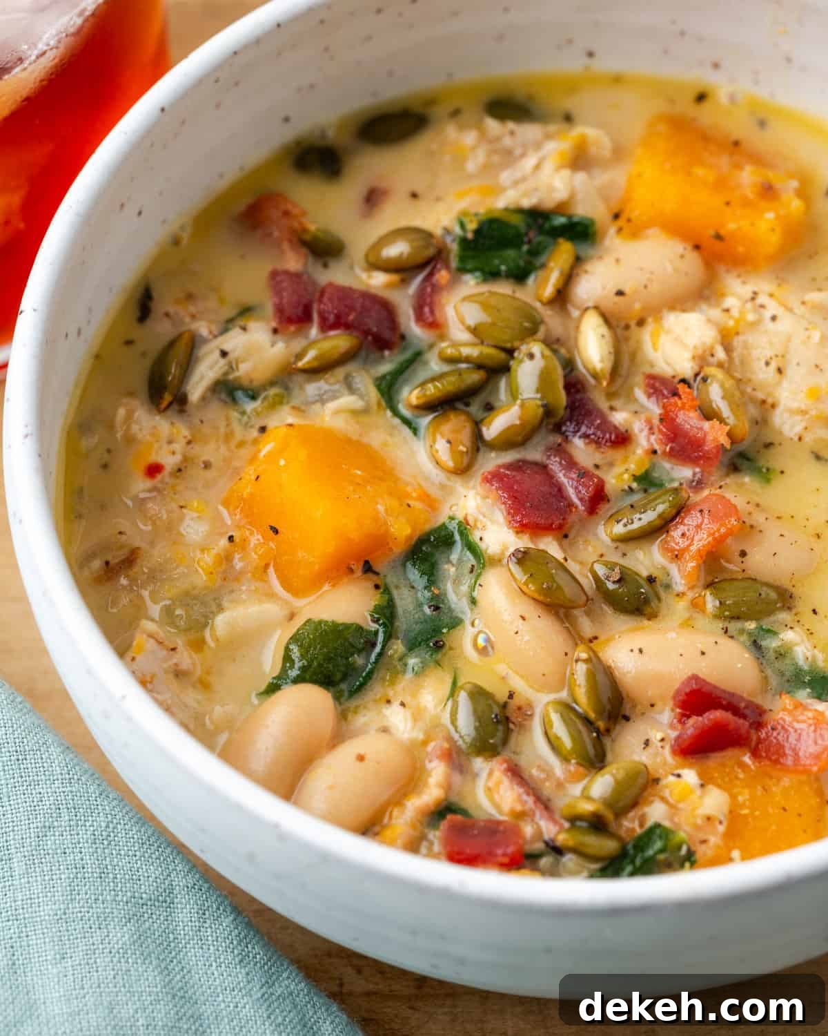 Creamy Chicken and Butternut Squash Soup Recipe 2 A bowl of creamy chicken butternut squash soup topped with pieces of bacon and roasted pepitas.