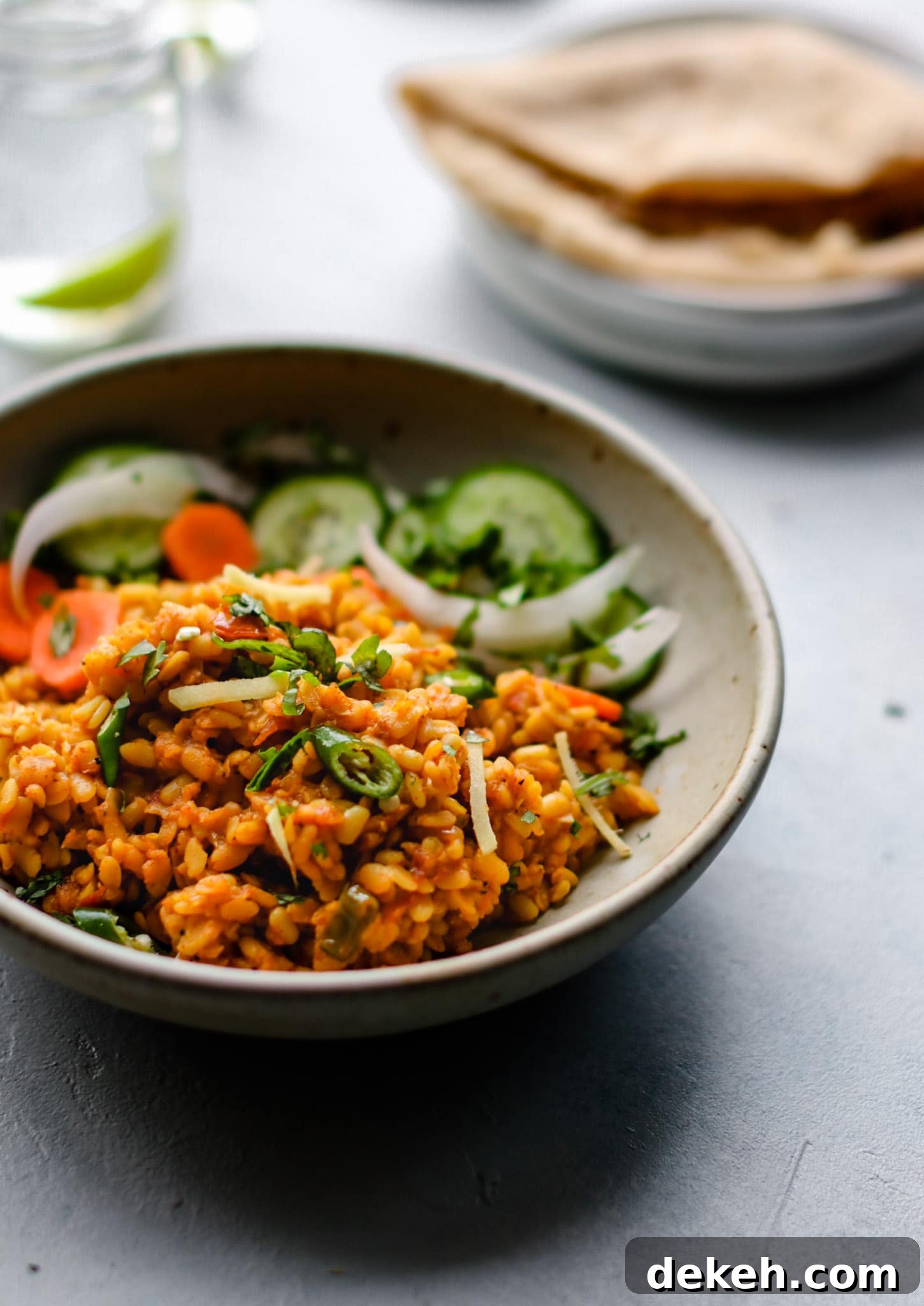 Authentic Pakistani Maash (Urad) Dal Recipe 4 Close up of a bowl of Mash ki Daal (Urad Dal) with cucumbers and carrots garnished with sliced onions, green chilies and cilantro.