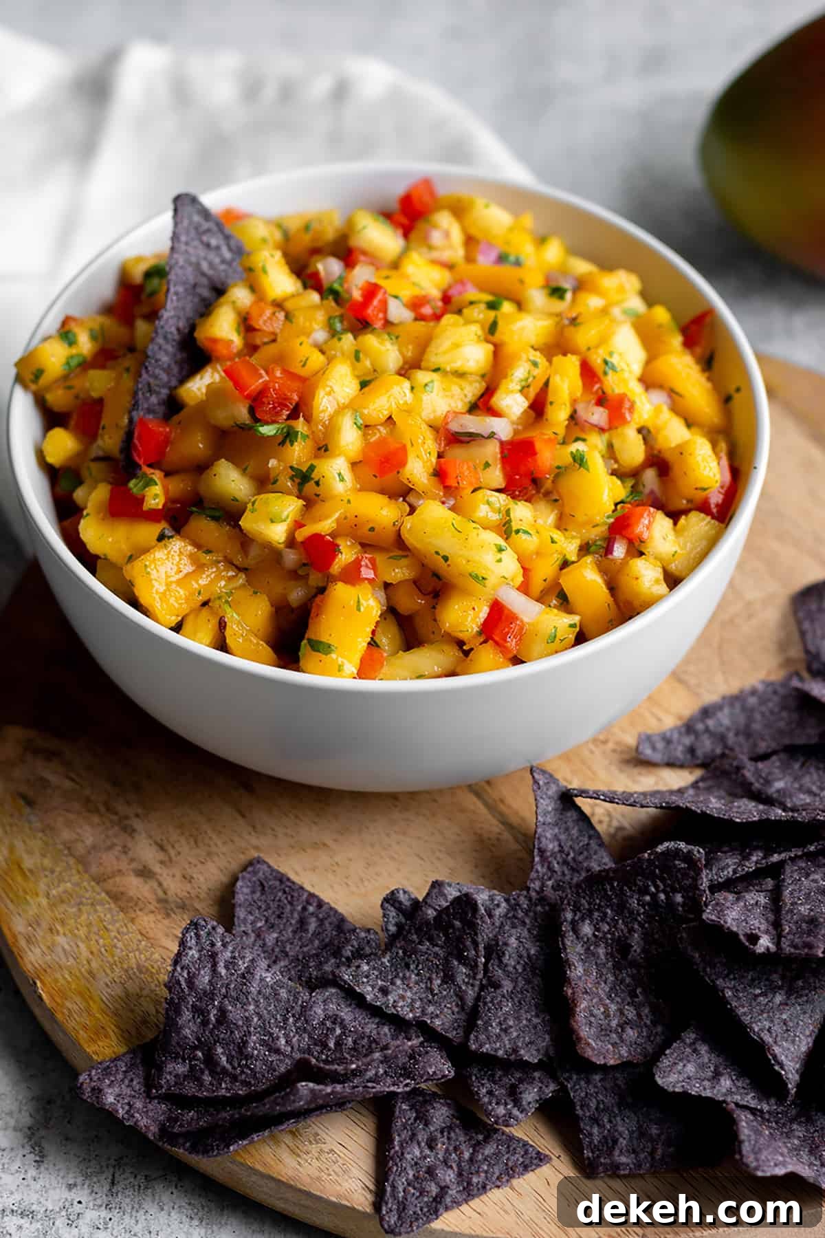 Zesty Mango and Pineapple Salsa with Lime and Cilantro 2 White bowl with diced mangos, pineapples and blue corn tortilla chips.