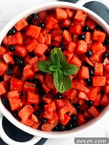 A white serving tray with cubed watermelon, blueberries and fresh mint on top.