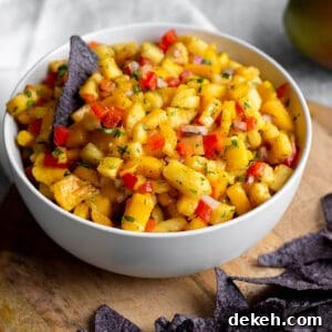 Zesty Mango and Pineapple Salsa with Lime and Cilantro 10 A bowl with diced mangos, pineapples and blue corn tortilla chips on a wooden board.